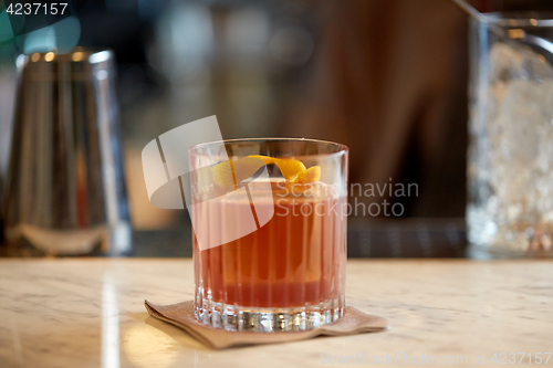 Image of glass of cocktail with orange peel at bar