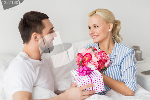 Image of happy couple with gift box in bed at home