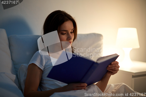 Image of young woman reading book in bed at night home