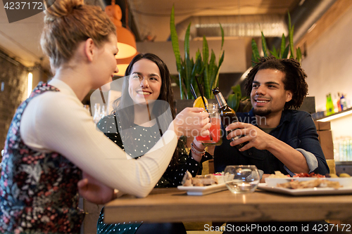 Image of happy friends clinking drinks at bar or cafe