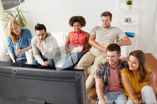 Image of happy friends with popcorn watching tv at home