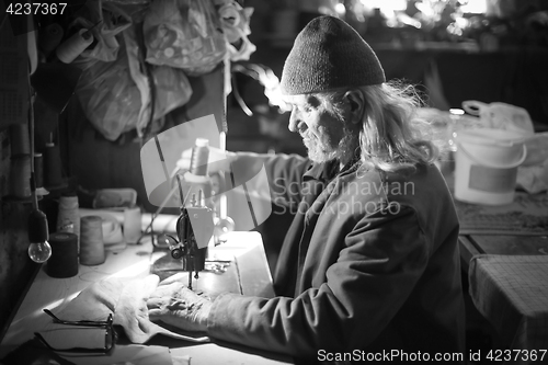 Image of Old man sewing cloth bw