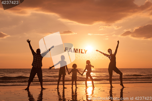 Image of Happy family standing on the beach at the sunset time.