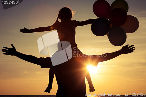 Image of Father and daughter with balloons playing on the beach at the su