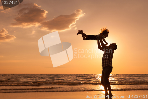 Image of Father and son playing on the beach at the sunset time.