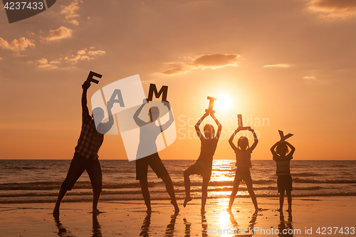 Image of Happy family standing on the beach at the sunset time.