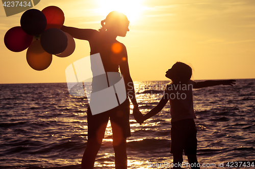 Image of Mother and daughter playing on the beach at the sunset time. 