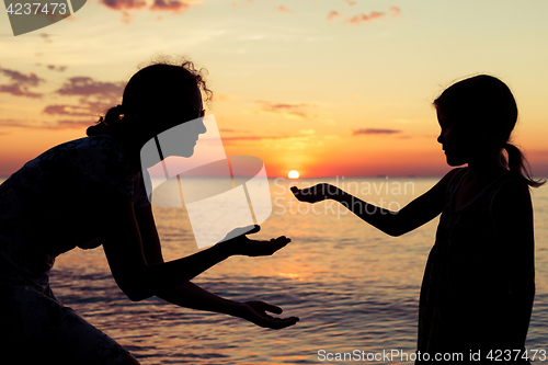 Image of Mother and daughter playing on the beach at the sunset time.