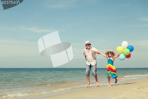 Image of Father and daughter with balloons playing on the beach at the da