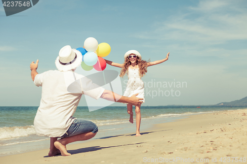 Image of Father and daughter with balloons playing on the beach at the da