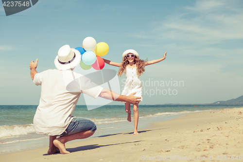 Image of Father and daughter with balloons playing on the beach at the da