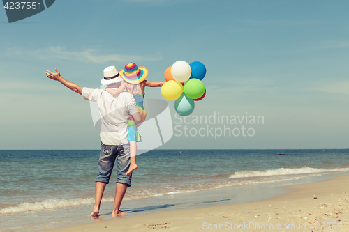 Image of Father and daughter with balloons playing on the beach at the da