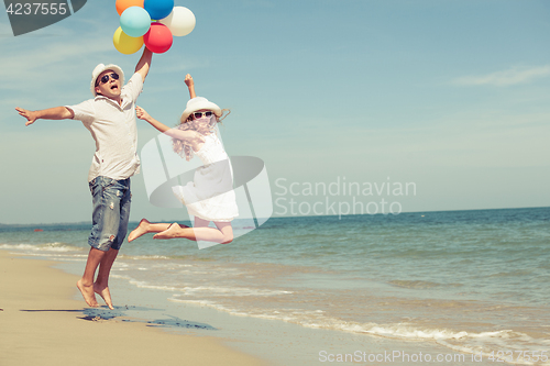 Image of Father and daughter with balloons playing on the beach at the da