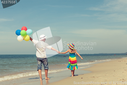 Image of Father and daughter with balloons playing on the beach at the da