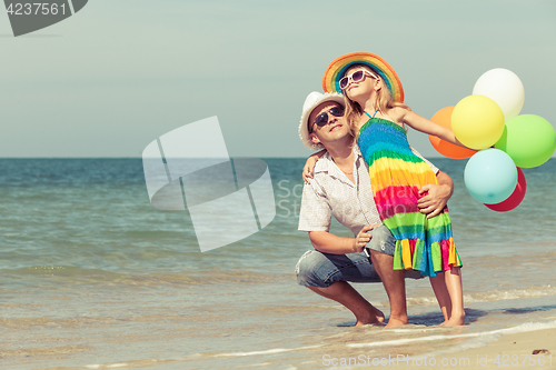 Image of Father and daughter with balloons playing on the beach at the da