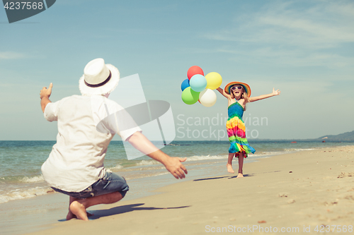 Image of Father and daughter with balloons playing on the beach at the da