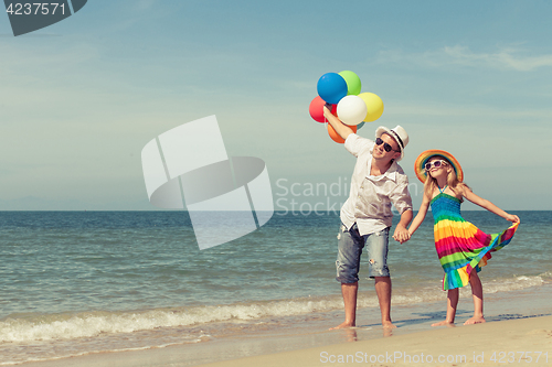 Image of Father and daughter with balloons playing on the beach at the da