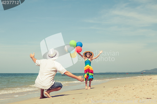Image of Father and daughter with balloons playing on the beach at the da
