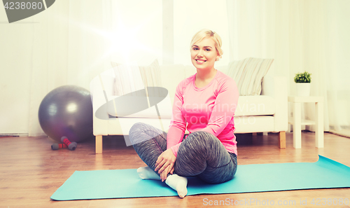 Image of happy woman sitting on mat at home