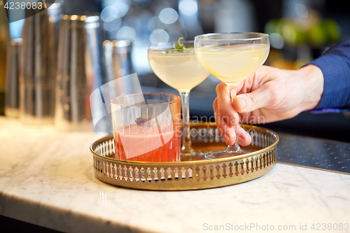 Image of bartender with glasses of cocktails at bar
