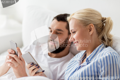 Image of happy couple with smartphones in bed at home