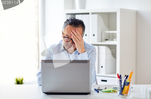 Image of businessman in eyeglasses with laptop at office