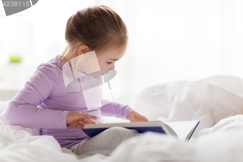 Image of happy little girl reading book in bed at home