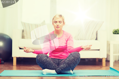 Image of happy woman stretching leg on mat at home