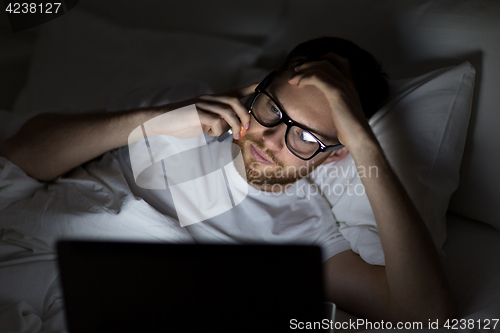 Image of man with laptop calling on smartphone at night