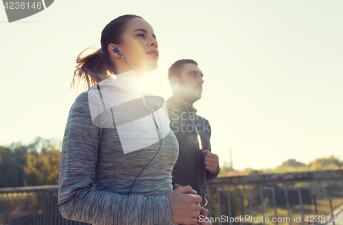 Image of happy couple with earphones running outdoors