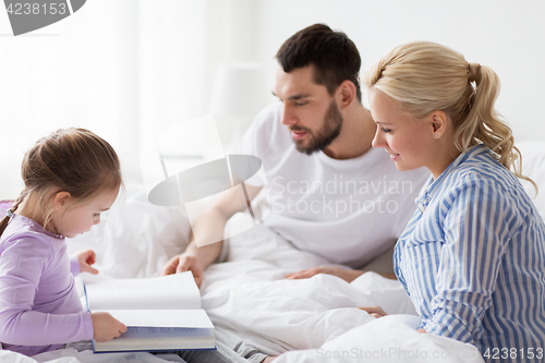 Image of happy family reading book in bed at home