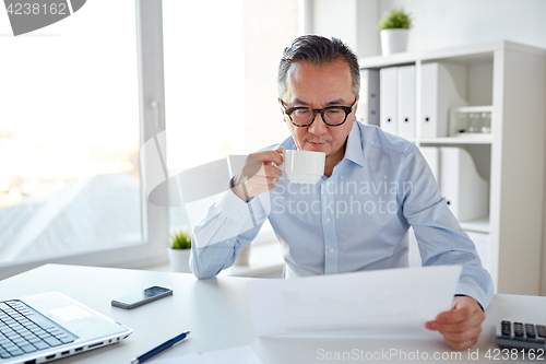 Image of businessman with papers drinking coffee at office
