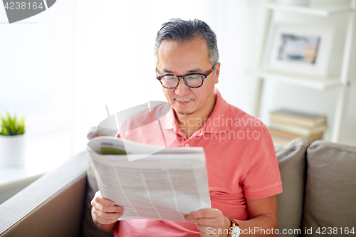 Image of happy man in glasses reading newspaper at home