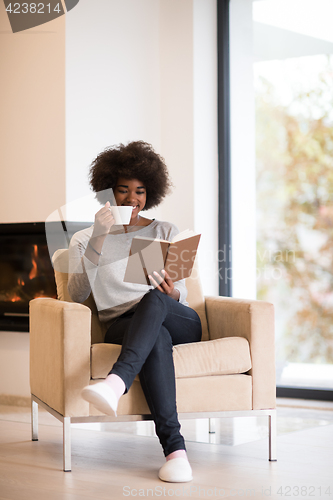 Image of black woman reading book  in front of fireplace