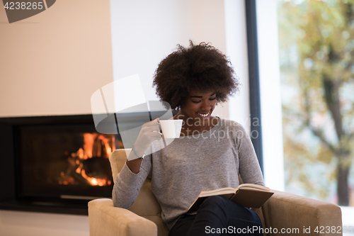 Image of black woman reading book  in front of fireplace