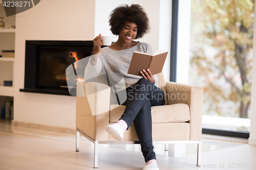 Image of black woman reading book  in front of fireplace