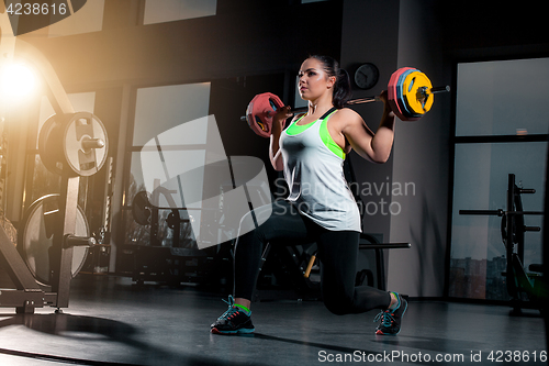 Image of Fit young woman lifting barbells looking focused, working out in a gym