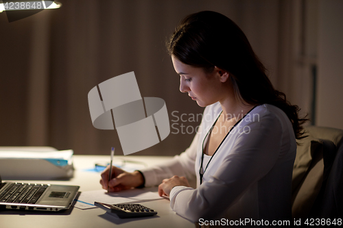 Image of woman with calculator and papers at night office