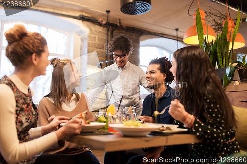 Image of happy friends eating and drinking at restaurant