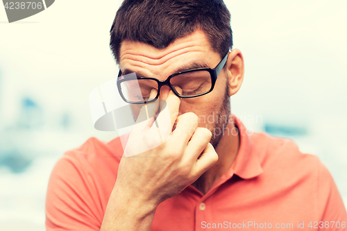 Image of tired man in eyeglasses rubbing eyes at home