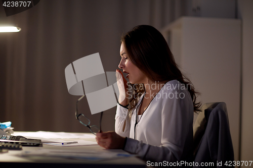 Image of tired woman with glasses yawning at night office