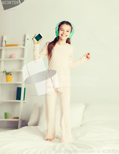 Image of girl jumping on bed with smartphone and headphones