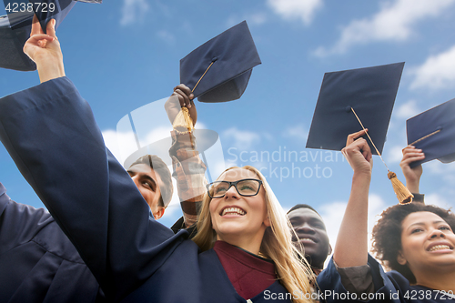 Image of happy bachelors waving mortar boards over sky