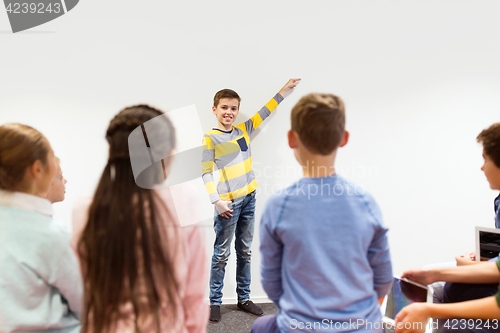 Image of happy student boy showing something at white wall
