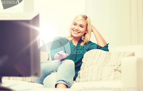 Image of smiling woman with remote watching tv at home