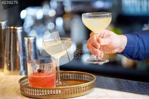 Image of bartender with glasses of cocktails at bar