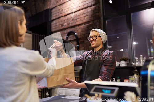 Image of woman taking paper bag from seller at cafe