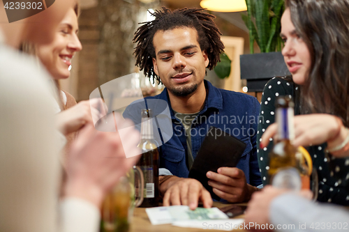 Image of friends with drinks, money and bill at bar