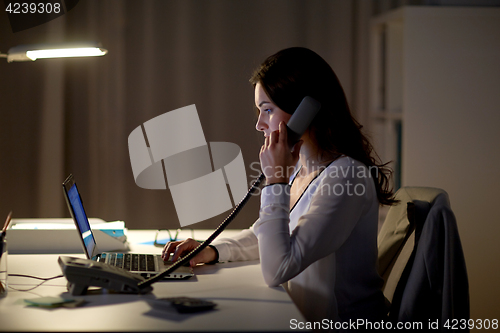 Image of woman with laptop calling on phone at night office