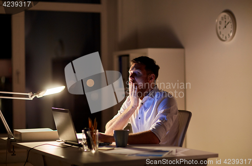 Image of man with laptop and coffee working at night office